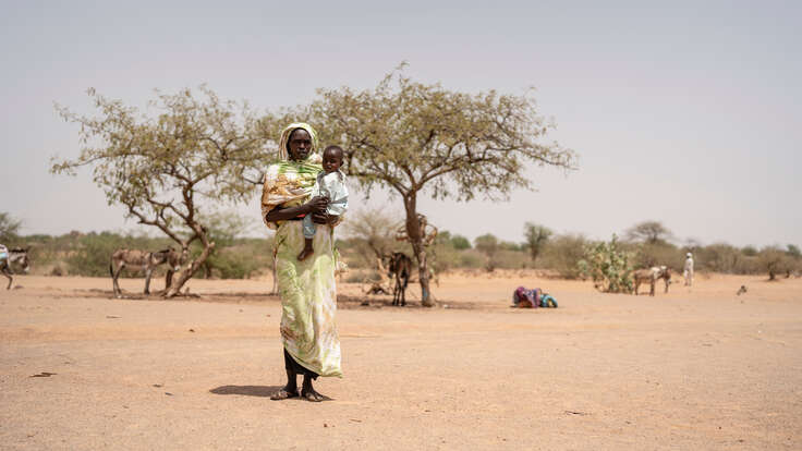 En kvinna står och håller sitt barn i famnen i Tchad